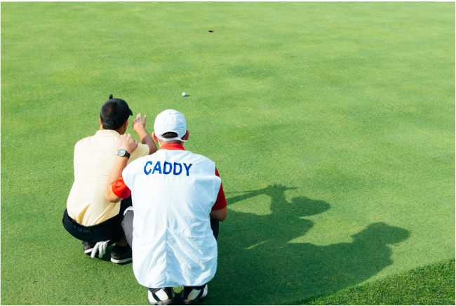 Golf instructor and caddy reading a putt together, focusing on strategy and success in teaching golf.