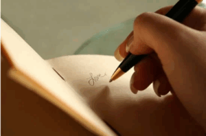 Hand writing in a journal with a pen, capturing thoughts and reflections.