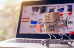 Mini shopping cart with cardboard boxes on a laptop keyboard, symbolizing turning ideas into digital products and online sales.